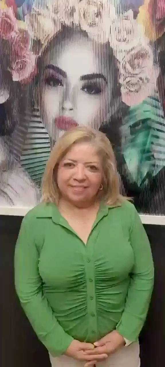 Paciente sonriente de cabello rubio a la altura de los hombros y blusa verde, frente a un mural de retrato floral