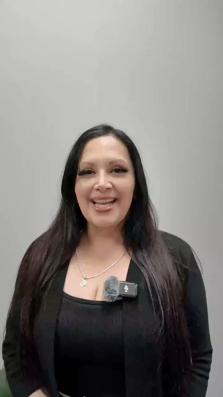 Paciente sonriente de cabello largo y oscuro, con blusa negra y micrófono de solapa