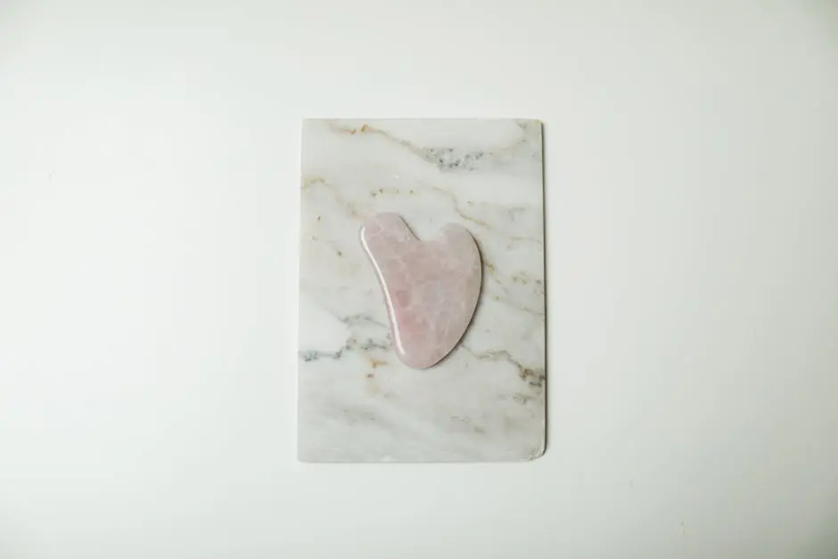 A rose quartz gua sha tool elegantly placed on a white marble slab, perfect for skincare routines.